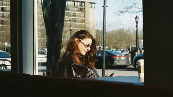 Woman looking at phone inside cafe with cars outside