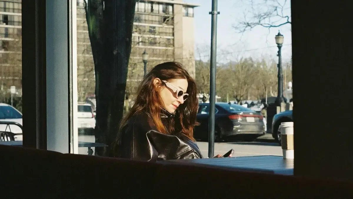 Woman looking at phone inside cafe with cars outside