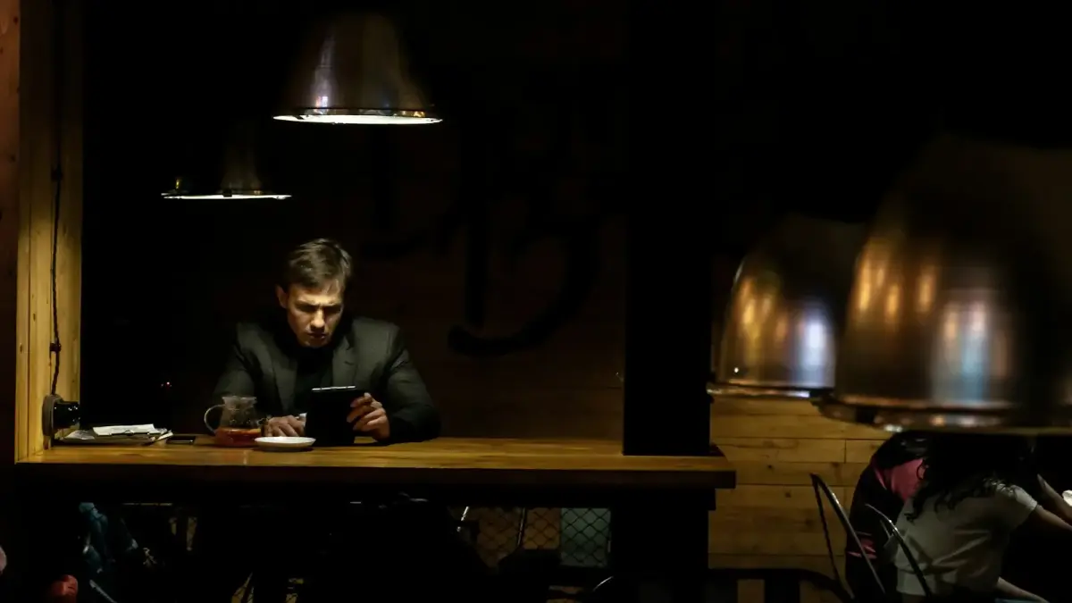 man in black suit jacket sitting beside brown wooden table
