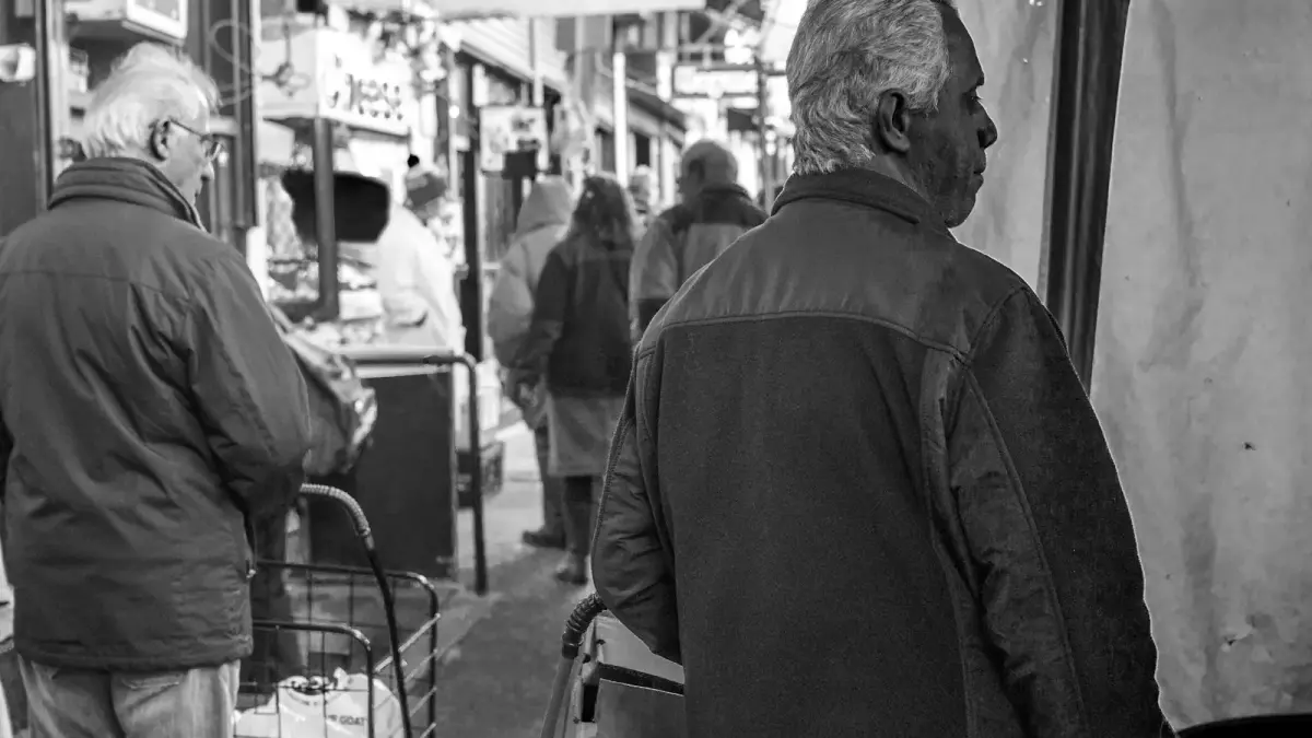 man in black jacket standing near people walking on street in grayscale photography