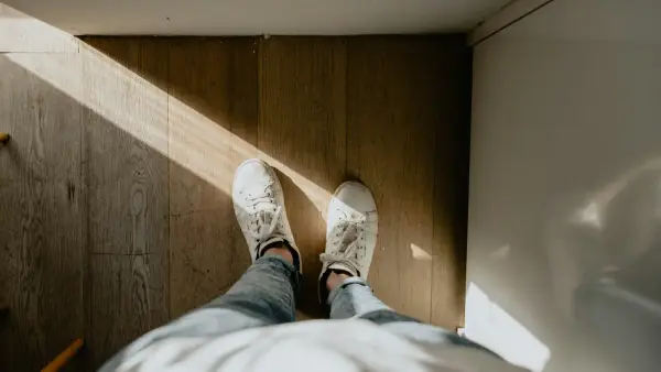 person wearing pair of white shoes standing on brown wood parquet floor