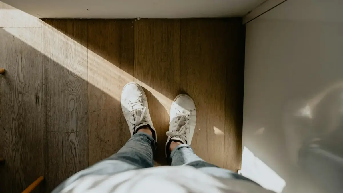 person wearing pair of white shoes standing on brown wood parquet floor