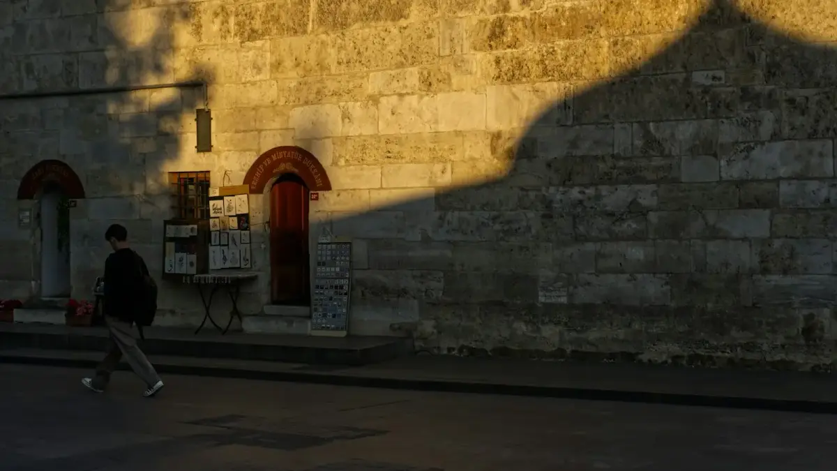 Man walks past stone building with arched doorways at sunset.