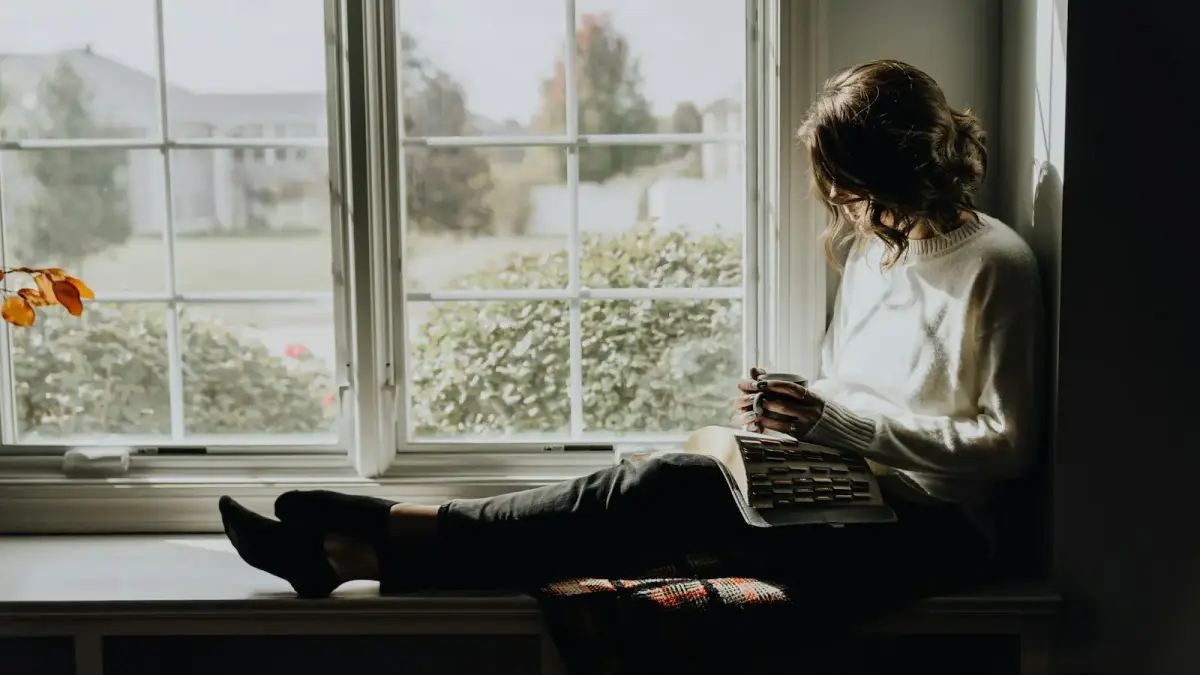 A woman sitting on a window sill reading a book