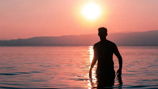 silhouette of man standing on water during sunset