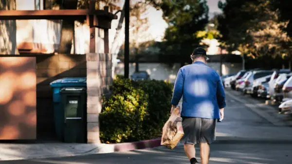 man in blue dress shirt and brown pants standing on sidewalk during daytime