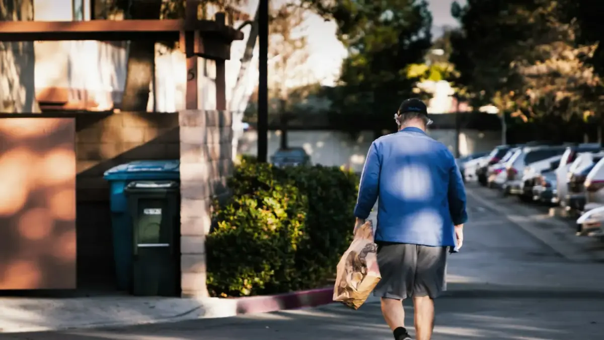 man in blue dress shirt and brown pants standing on sidewalk during daytime