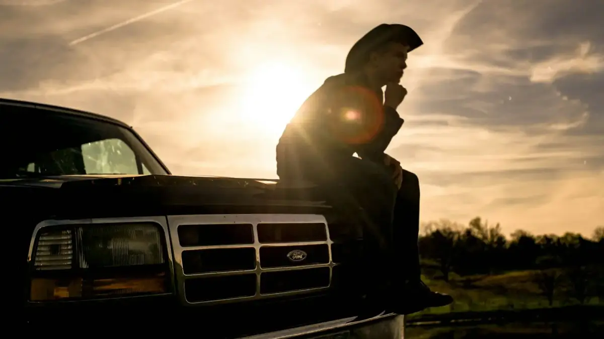 man in black jacket and black cap sitting on black car hood during daytime