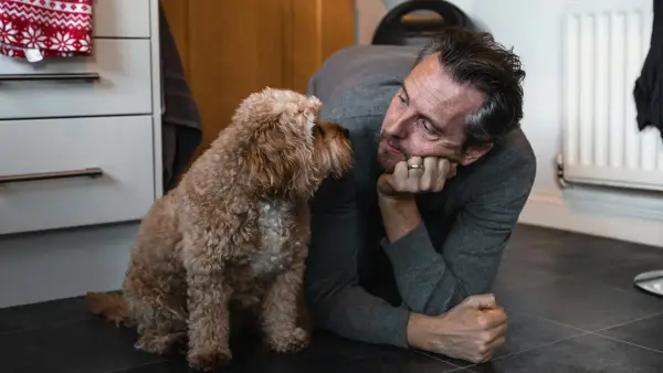 man in black sweater holding brown long coated small dog