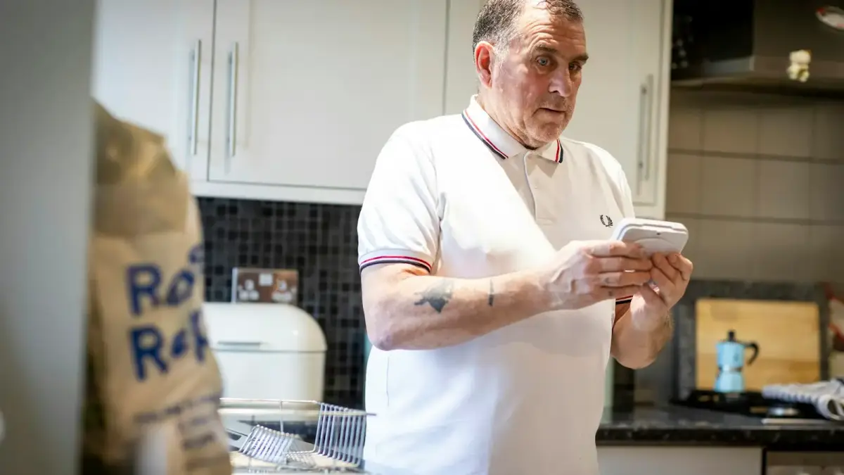 a man standing in a kitchen looking at a cell phone