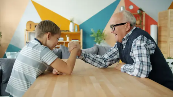 Grandfather and grandson arm wrestling at table