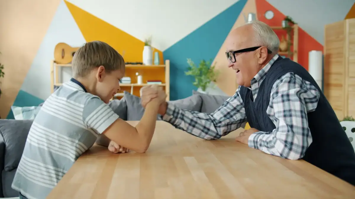 Grandfather and grandson arm wrestling at table