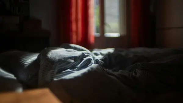 An unmade bed in a dark room with red curtains