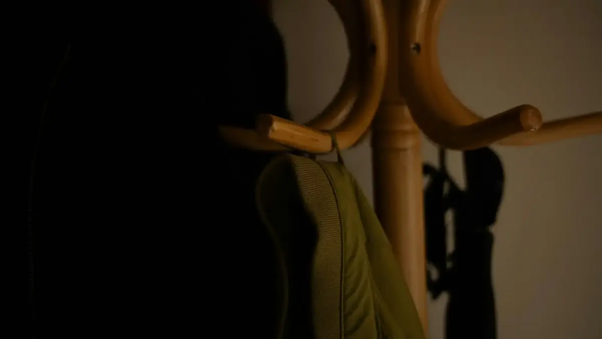 Wooden coat rack with a green jacket in dim light.