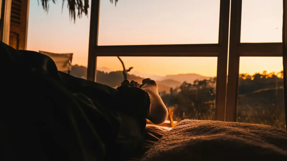 person lying on bed with view of sunset