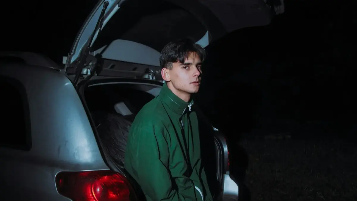 Young man sitting in the open trunk at night.