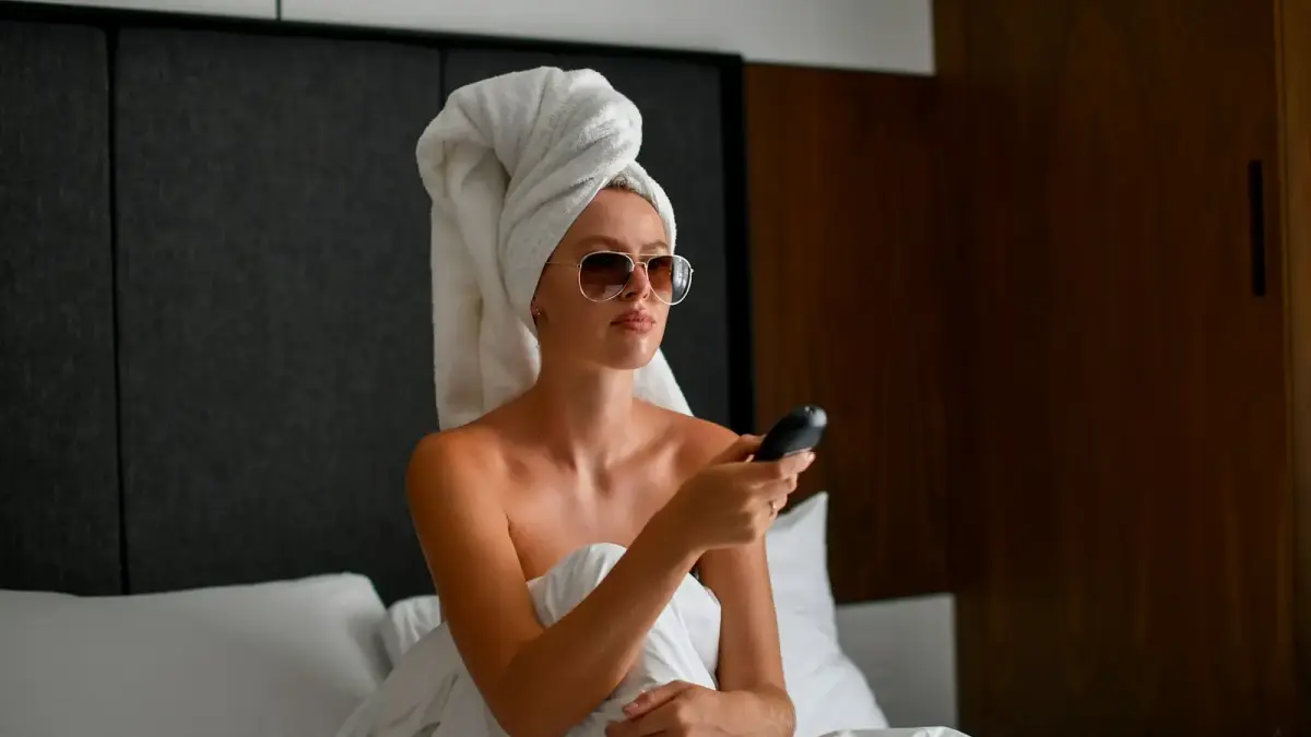 Woman in towel holding remote control in bed