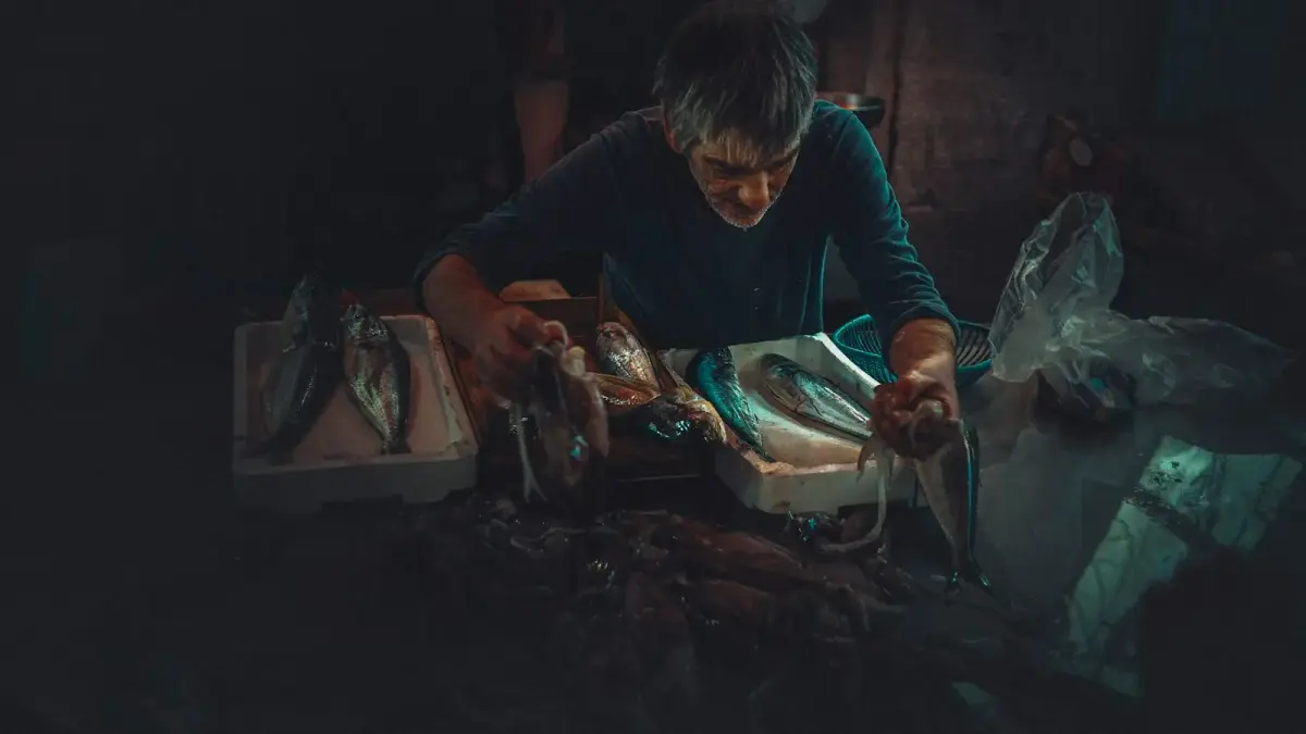 man in black long sleeve shirt holding knife slicing fish