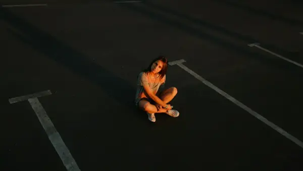 woman in gray tank top and blue denim shorts sitting on black asphalt road during daytime
