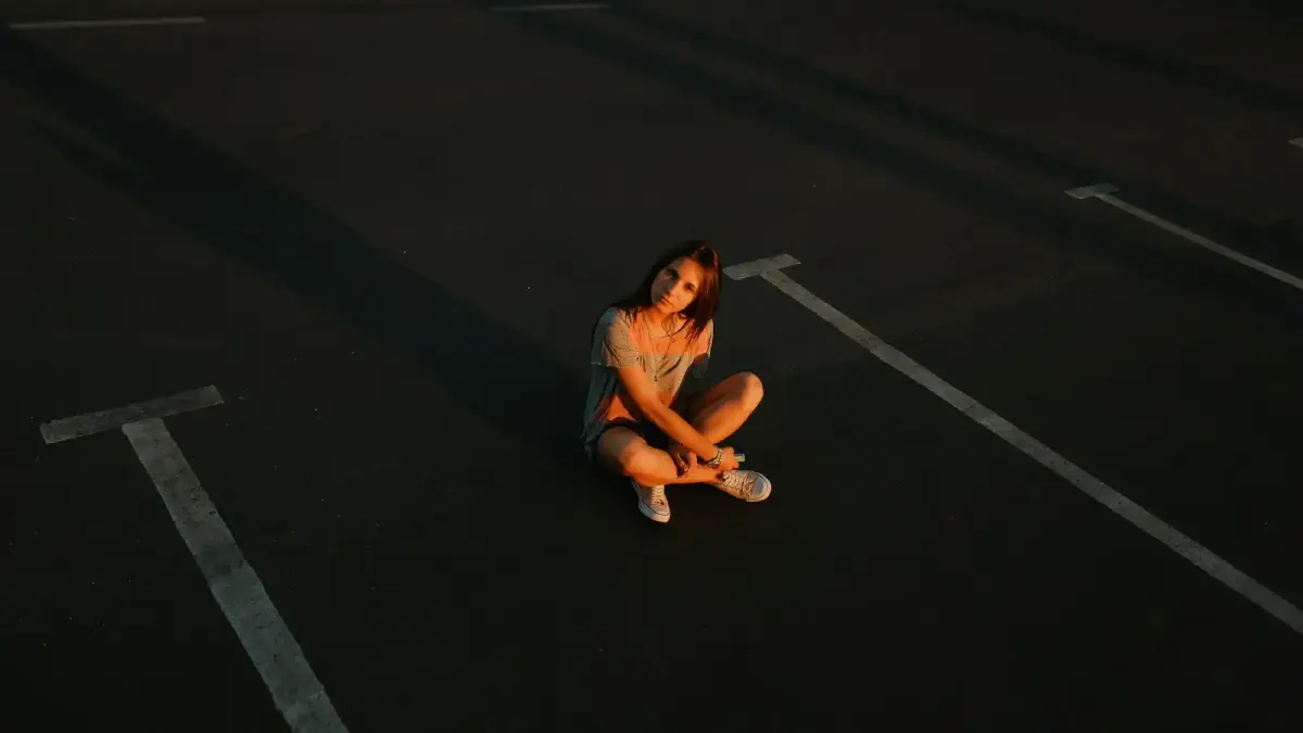 woman in gray tank top and blue denim shorts sitting on black asphalt road during daytime