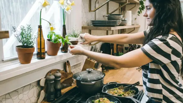 woman standing in front of cooking range holding flower's leaves
