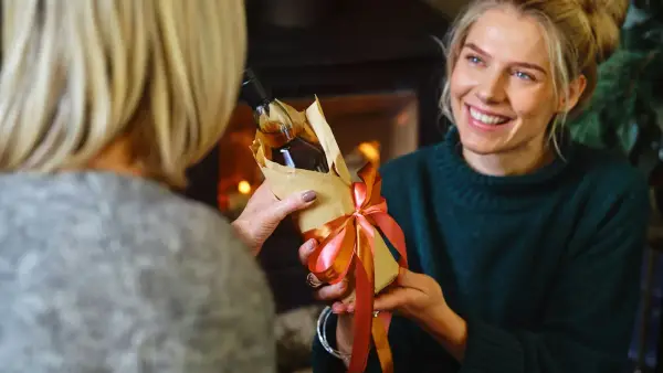 a woman holding a wrapped present in front of another woman