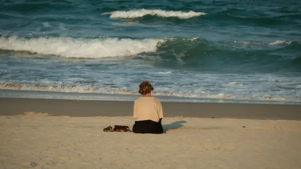 Woman sitting on beach facing the ocean waves