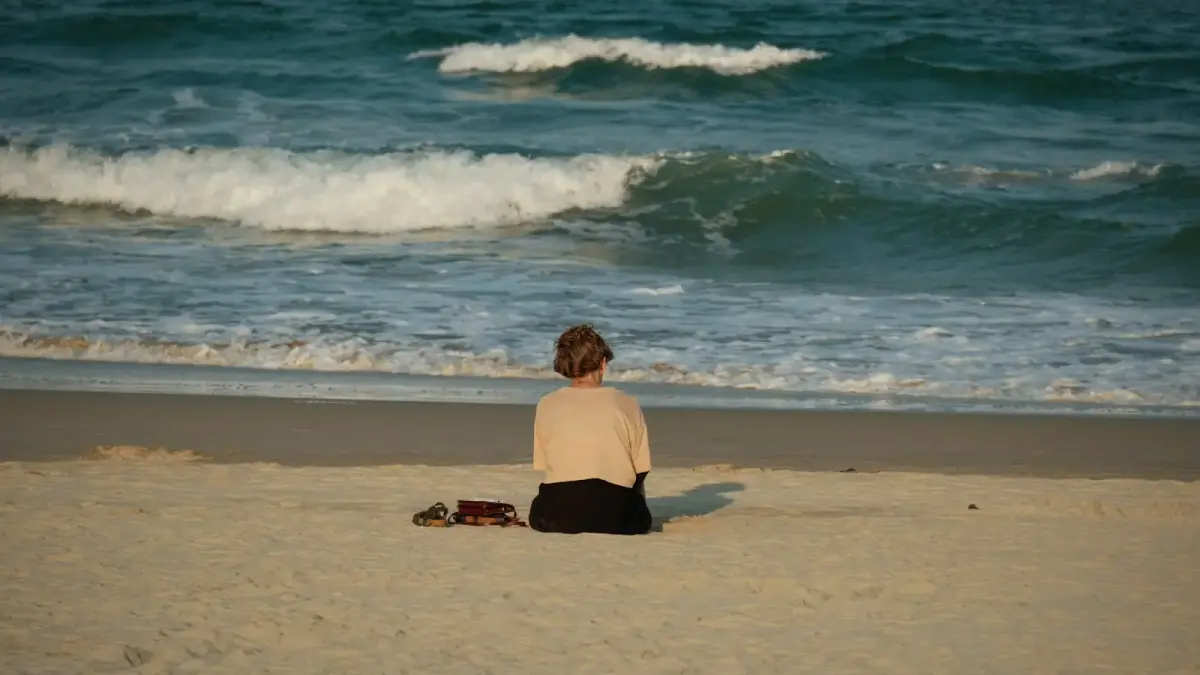 Woman sitting on beach facing the ocean waves
