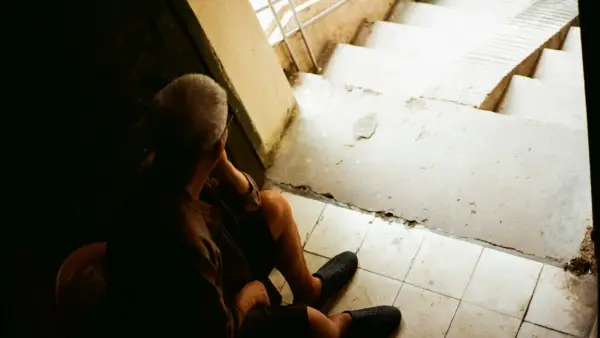 Elderly man sitting on stairs, looking down.