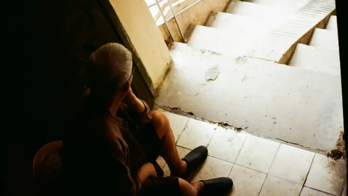 Elderly man sitting on stairs, looking down.