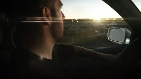 Man driving car towards sunset with lens flare