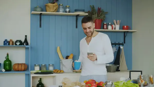 Man smiling while holding coffee and phone in kitchen