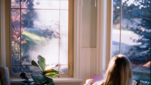 Woman reading by window with autumn foliage outside
