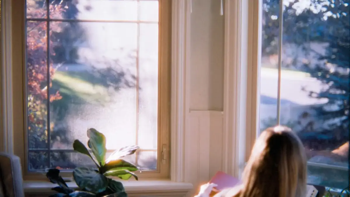 Woman reading by window with autumn foliage outside