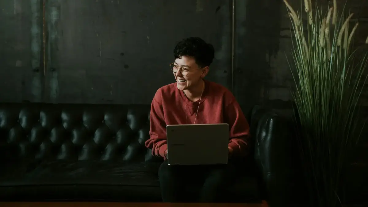 smiling man using laptop computer while sitting on black leather sofa