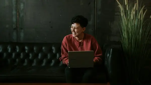 smiling man using laptop computer while sitting on black leather sofa
