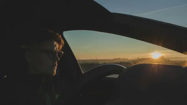 A woman sitting alone in a parked car, composing herself in soft light before going inside